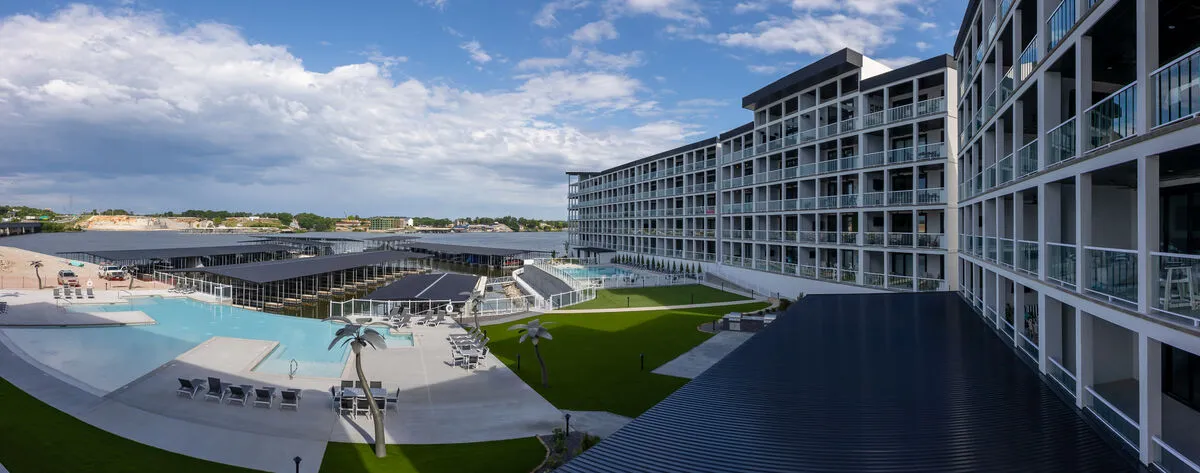 The image showcases the exterior of the Topsider condo, highlighting a sparkling swimming pool bordered by comfortable lounge seating and a landscaped lawn, all set against the backdrop of a glowing sunset over Lake of the Ozarks. Guests are depicted relaxing poolside, enjoying the tranquil and social atmosphere.