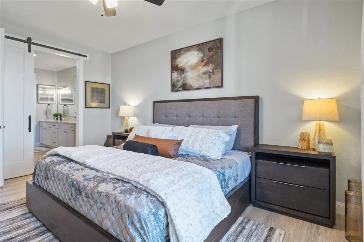 A cozy bedroom with a comfortable bed dressed in plush bedding, a nightstand with a lamp, and soothing wall art. Soft lighting and a gentle color palette enhance the sense of tranquility and comfort.