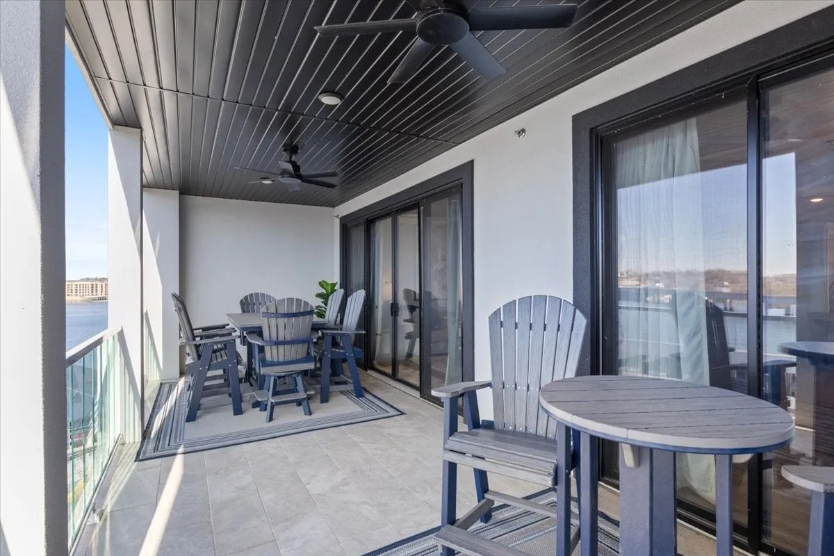 A tranquil outdoor dining and lounge area features adirondack chairs and a dining table, arranged to maximize views of the water. Sliding glass doors connect the space seamlessly to the interior, blending indoor comfort with outdoor relaxation.
