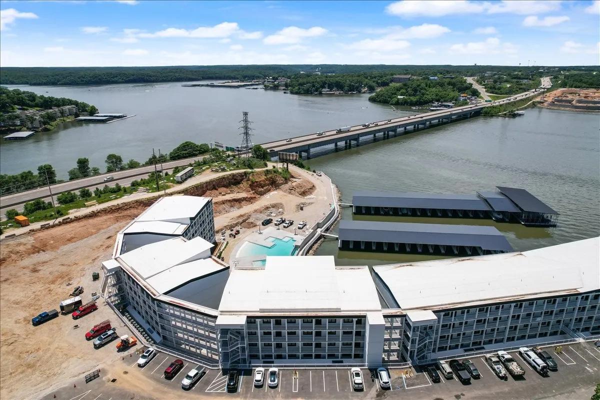 A scenic exterior shot showcasing the sparkling lake, the building's modern architecture, a bridge, and the adjacent parking area. The expansive water and surrounding landscape hint at a variety of outdoor activities available just steps from the property.