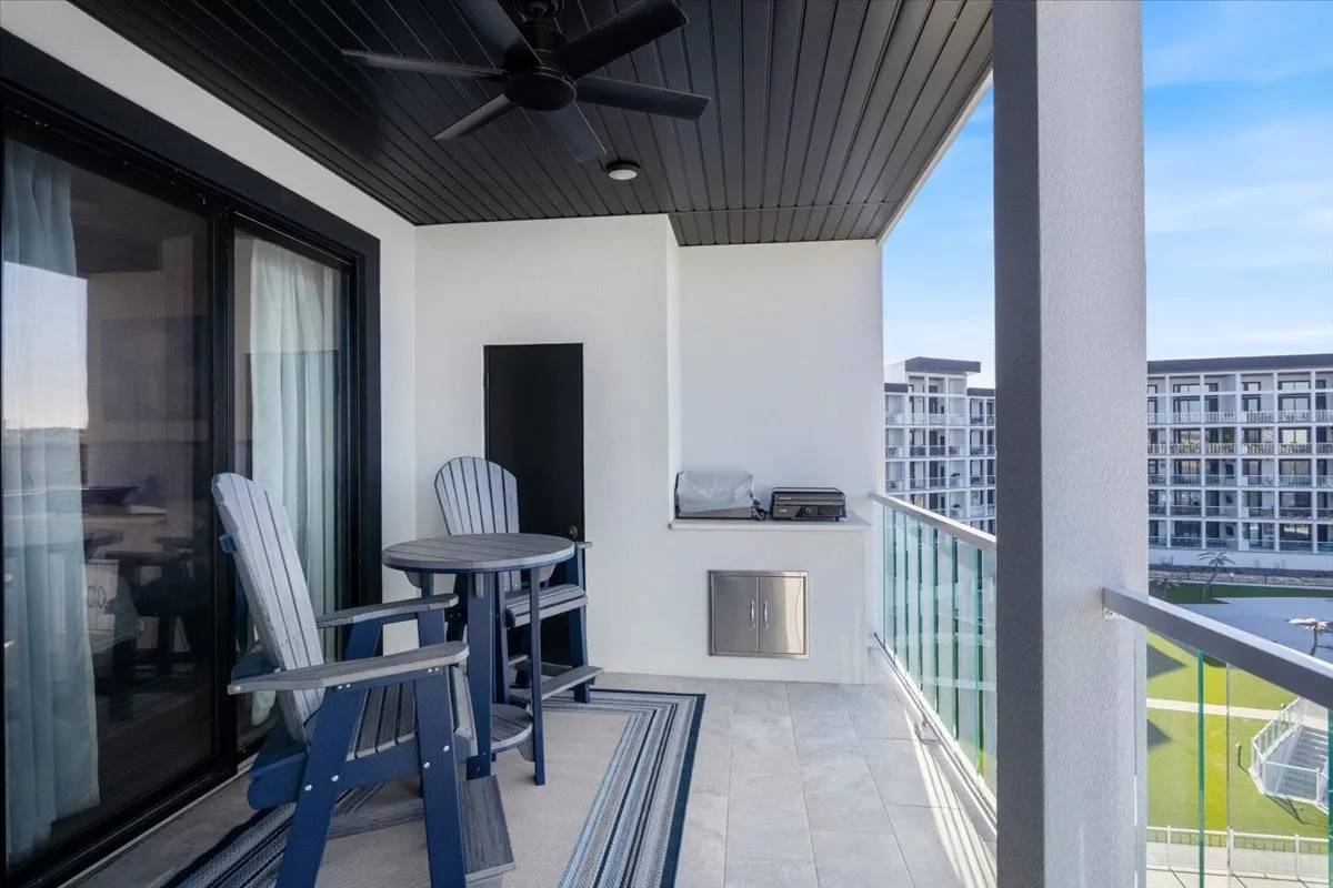 This image showcases a stylishly furnished balcony with modern outdoor furniture, a glass railing, and an outdoor grill. The space is designed for both relaxation and entertaining, with clear sightlines out to the lake and main channel beyond.
